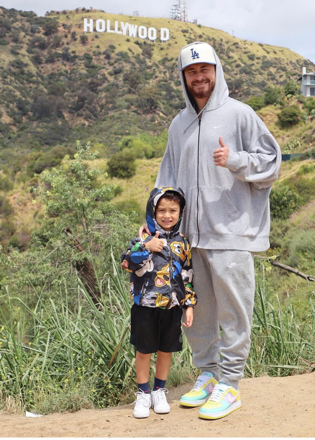 Pai e filho com boné do Dodgers em frente ao Hollywood Sign