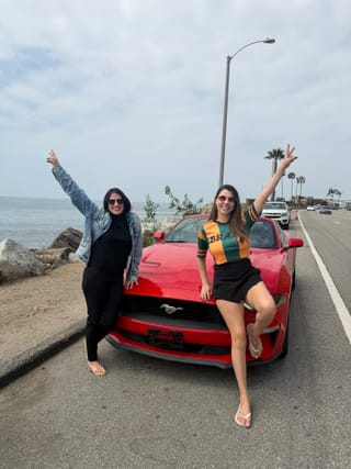 Amigas com Mustang vermelho na costa do Pacífico