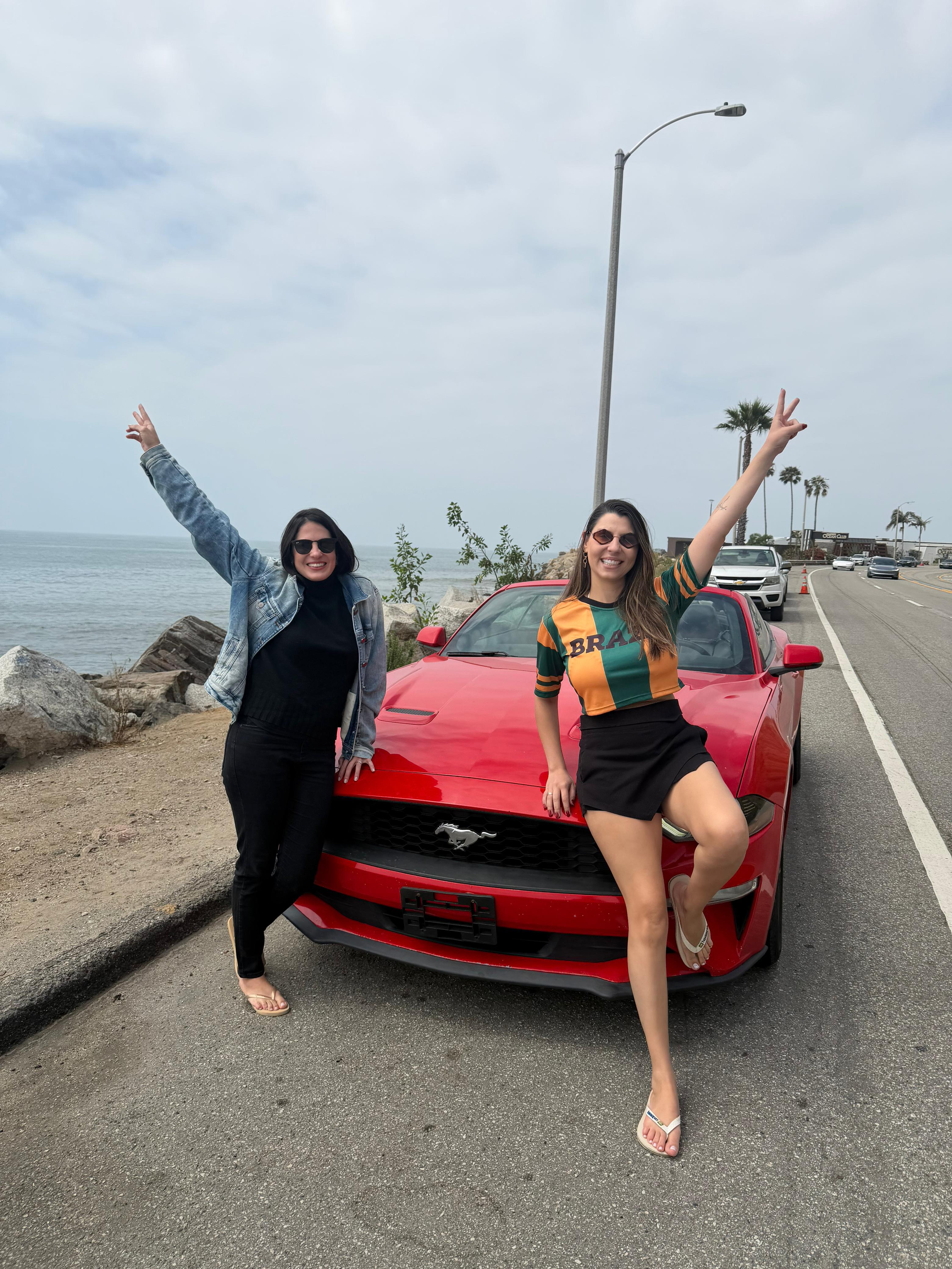 Amigas com Mustang vermelho na costa do Pacífico